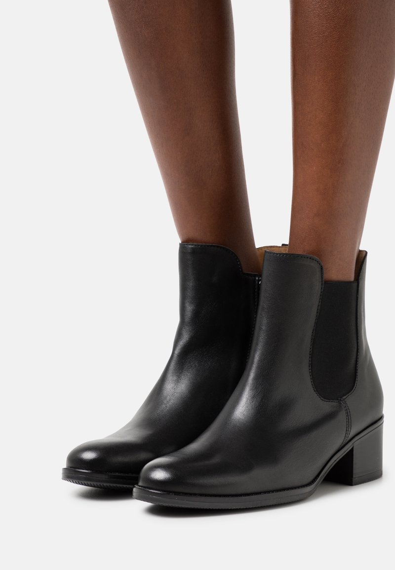 Botas de tobillo de cuero negro con paneles elásticos en los laterales, punteras redondeadas y un pequeño tacón cuadrado, que ofrecen un acabado liso y brillante.