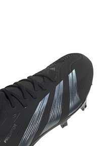 Scarpa da calcio nera con un design aerodinamico, caratterizzata da dettagli metallici argento e texture lungo la parte superiore. Chiusura con lacci visibile.