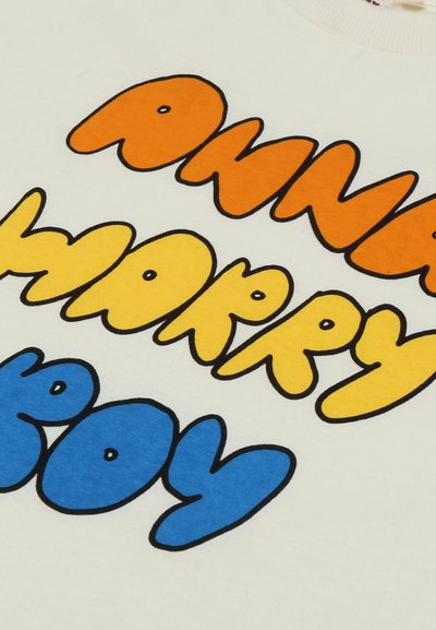 Texte en gras et arrondi en orange, jaune et bleu affichant "ama happy boy" sur un fond en tissu de couleur claire.
