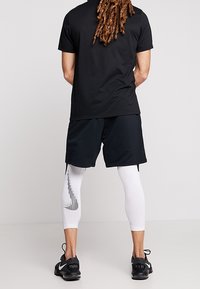 Black short-sleeve shirt, black shorts, and white compression leggings with black stripe pattern. Black athletic shoes with logo.