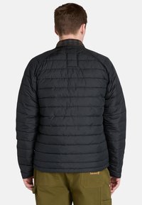 Chaqueta de plumas negra con un diseño acolchado, que presenta un cuello de cuadros. La tela es suave y ligera, con costuras horizontales y un corte relajado.