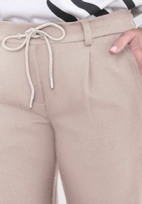 Kaki broek met een gladde textuur en een trekkoord in de taille, voorzien van een metalen aglet. Voorplooien geven structuur aan het ontwerp.