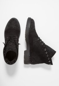 Botas de tobillo de ante negro con puntera con tachuelas, diseño de cordones y un tacón texturizado con ojales decorativos. Suela de goma.