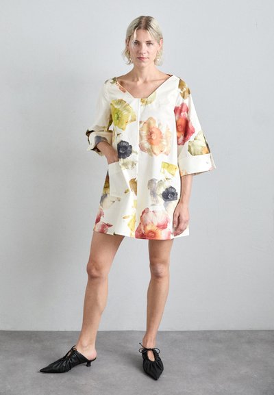 Vestido con estampado floral y mangas oversized, hecho de tela ligera, con escote en V y dos bolsillos laterales. Se lleva con mules negros.