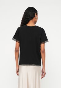 Črna bombažna majica s kratkimi rokavi, okrašena z prosojnim čipkastim trakom ob robu in robovih rokavov. Preprost, oprijet dizajn.