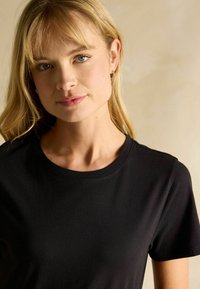 Melna kokvilnas T-kreklu ar apaļu kakla izgriezumu un īsām piedurknēm, ar gludu tekstūru un pieguļošu dizainu.