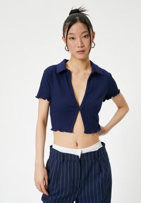 Marineblaue, taillierte Poloshirt mit gerippter Textur, kurzen, gerafften Ärmeln und Knopfverschluss, kombiniert mit gestreiften Hosen.