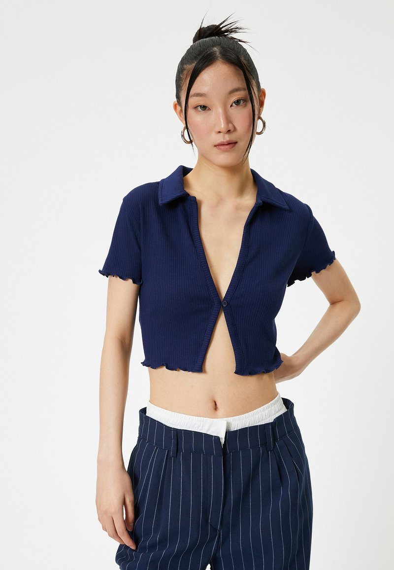 Marineblaue, taillierte Poloshirt mit gerippter Textur, kurzen, gerafften Ärmeln und Knopfverschluss, kombiniert mit gestreiften Hosen.