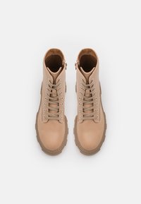 Bottes cheville en cuir beige à texture lisse, bout rond, design à lacets et fermeture éclair latérale pour un enfilage facile. Semelle épaisse en caoutchouc pour la stabilité.