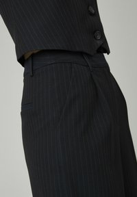 Gros plan sur un pantalon de costume noir à rayures avec une veste assortie boutonnée à la taille.