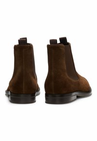 Brązowe zamszowe botki Chelsea z elastycznymi panelami bocznymi, płaskimi podeszwami i pętlami z tyłu ułatwiającymi zakładanie. Gładka faktura, czysty design.