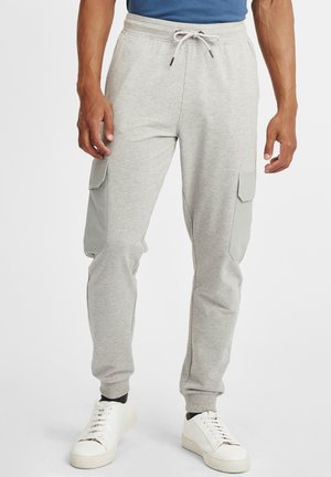 Light gray sweatpants with a tapered fit, adjustable waistband, and two side cargo pockets featuring gray accents. White sneakers complete the look.