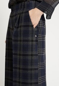 Mřížkové kalhoty v námořnické, černé a šedé barevné kombinaci. Obsahují postranní kapsy a dekorační prvek u švu kapsy.