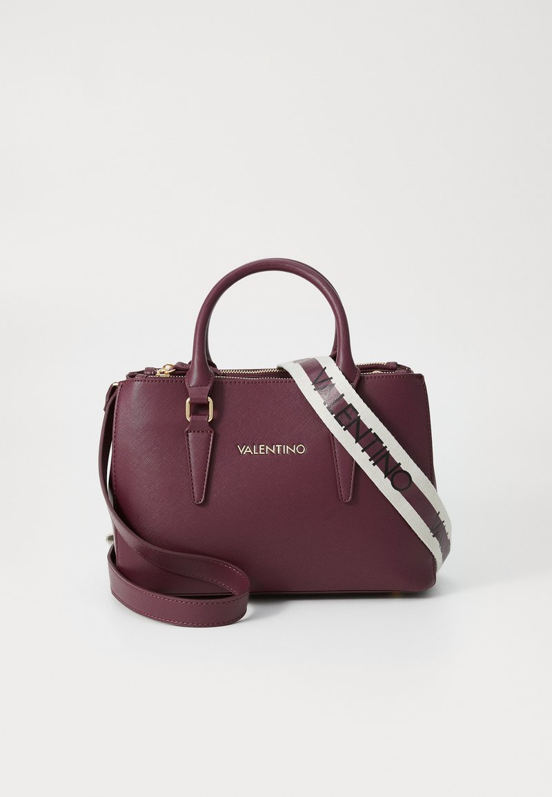 Burgundy leather handbag with dual handles, gold hardware, and detachable striped shoulder strap featuring the brand name in black.