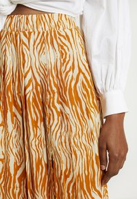 Jupe plissée orange et crème avec un motif à rayures zèbre, en tissu léger, dotée d'une taille haute et d'une texture douce.