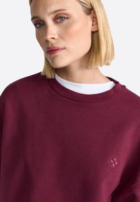 Sweatshirt bordeaux avec un col crew côtelé et un logo brodé. Tissu doux avec une texture lisse, mettant en valeur une coupe décontractée.