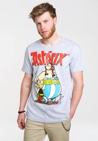 Graues T-Shirt mit einem bunten, cartoonhaften Grafik von Asterix und Obelix, mit bold roten Lettern "Asterix" über den Figuren.