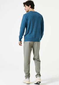 Blauwe gebreide trui met een ronde halslijn, gecombineerd met lichtgrijze broek en beige sportschoenen. De outfit heeft een ontspannen pasvorm.