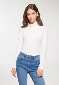 Biała, długi rękaw, golf dopasowany w stylu, gładka struktura, w połączeniu z niebieskimi dżinsami o wysokim stanie z kieszeniami i zapięciem na guziki z przodu.