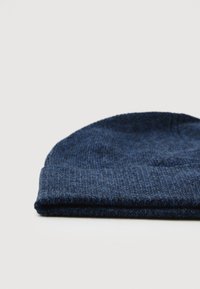 Cappello di lana blu scuro a maglia ripiegato nella parte inferiore, appoggiato su una superficie bianca.