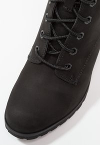 Bottine en daim noir à bout rond, avec surface texturée, six œillets et lacets noirs. Semelle en caoutchouc noir avec motif antidérapant.