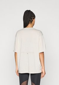 Φαρδιά oversized μπλούζα σε ανοιχτό μπεζ χρώμα με κοντά μανίκια. Διαθέτει εκτυπωμένο κείμενο κοντά στο κάτω μέρος και στρογγυλή λαιμόκοψη. Απαλή υφή υφάσματος.