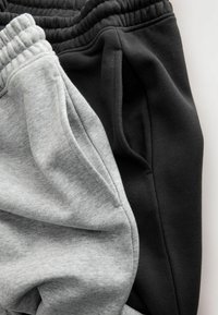 Deux paires de pantalons de survêtement : une grise et une noire, dotées de ceintures élastiques, d'une texture en coton doux et de poches latérales pour le rangement.