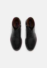 Botas de tobillo de cuero negro con diseño de cordones, detalle de cremallera y un interior marrón. Textura suave y forma de punta redonda.