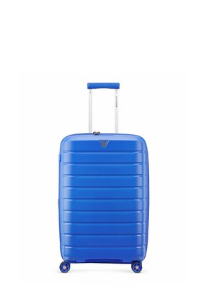 Valise rigide bleue avec des rainures horizontales, quatre roues et une poignée télescopique prolongée sur fond blanc.