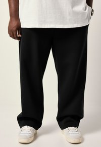 Zwarte, loszittende broek gemaakt van gladde stof, met een rechte pijpontwerp en minimalistische details, gecombineerd met witte sneakers.