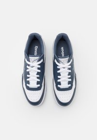 Pár modro-bílých tenisek Reebok se bílými tkaničkami, logo značky na jazyku a po stranách, zobrazeno z vrchního pohledu na bílém pozadí.