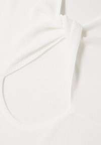 Tissu tricoté blanc avec un détail de nœud au centre, présentant une texture lisse et un col rond. Apparence douce et légère.