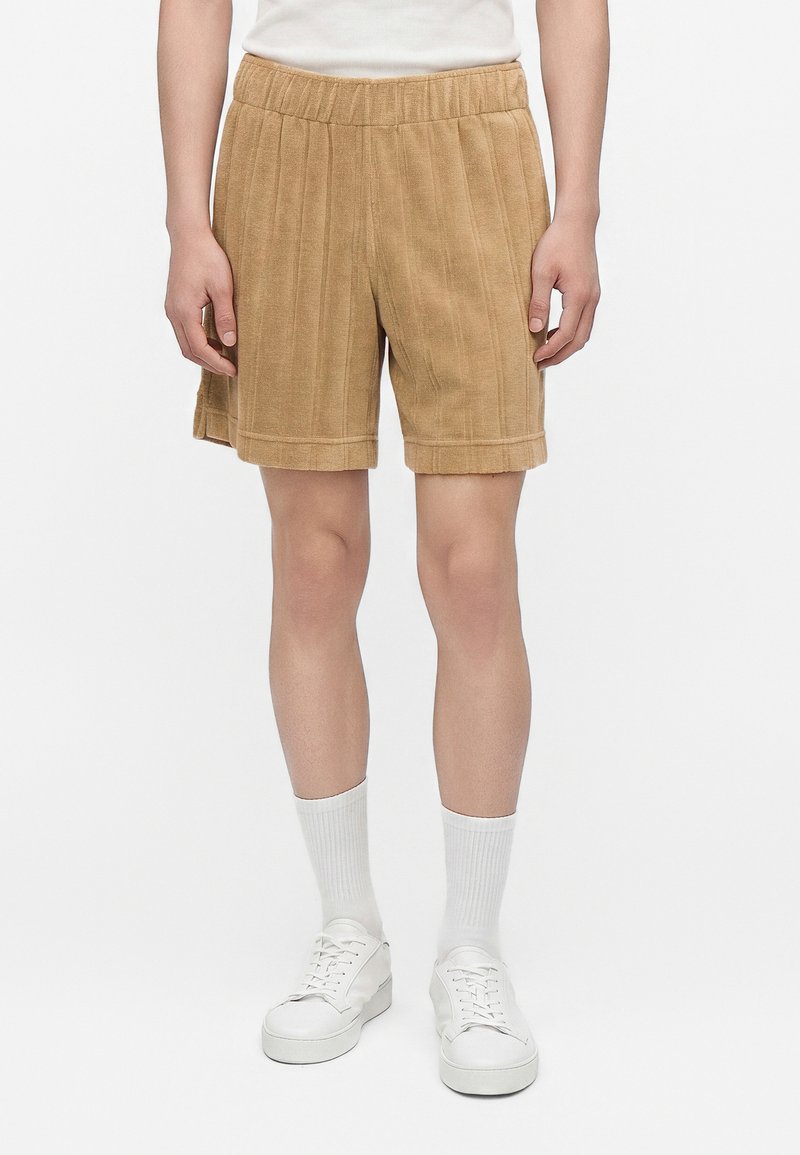 Person wearing beige ribbed shorts, white socks, and white lace-up sneakers, standing against a plain white background.