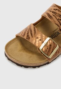 Sandales marron avec deux larges brides présentant un motif reptile métallisé texturé. Une boucle en métal doré accentue la bride ajustable.