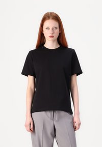 Sort kortærmet t-shirt lavet af glat stof, med rund hals og afslappet pasform, parret med lysegrå bukser.