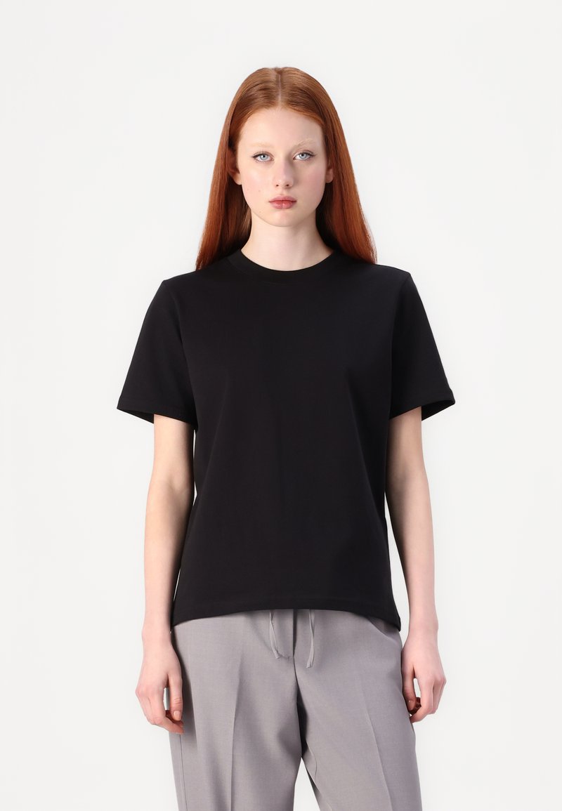 Sort kortærmet t-shirt lavet af glat stof, med rund hals og afslappet pasform, parret med lysegrå bukser.