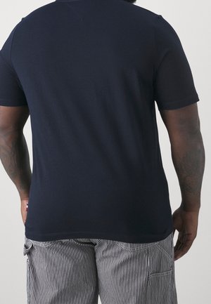 Hombre visto desde atrás con una camiseta de manga corta azul marino lisa y pantalones a rayas verticales en blanco y negro.