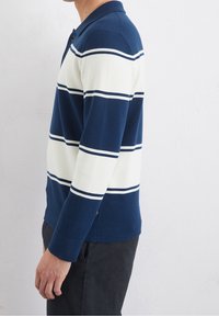 Polo a maniche lunghe a righe blu navy e bianche con colletto, caratterizzato da righe orizzontali e texture a maglia. Spacco laterale all'orlo.