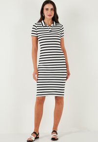 Mustavalkoraidallinen polo-mekko, jossa on lyhyet hihat, slim fit -malli, polvenpituinen, ribattua tekstiiliä ja klassinen kaulus. Yhdistetty mustiin sandaaleihin.