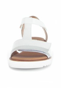 Sandale blanche avec une large lanière, accent argenté brillant et lanière ajustable à la cheville. Semelle intérieure en doux marron sur une semelle blanche.