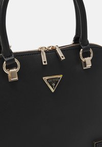 Schwarze synthetische Handtasche mit Hardware in Goldoptik, ausgestattet mit einem dreieckigen Logo, Reißverschluss und doppelten Griffen. Texturierte Oberflächendetails sind sichtbar.