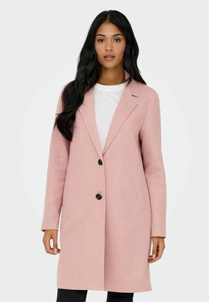 Manteau rose en mélange de laine avec une coupe blazer, col à revers cranté, deux poches avant et une fermeture à bouton unique, porté sur un haut blanc.