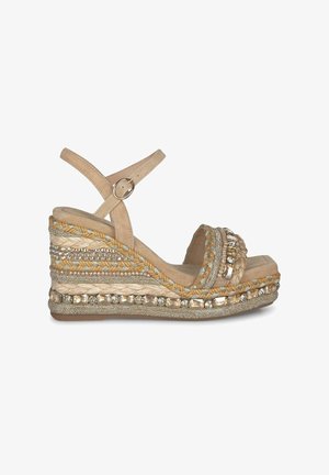Beige wedge sandal with braided jute design and decorative crystal accents. Features a wide strap and ankle buckle for secure fit.