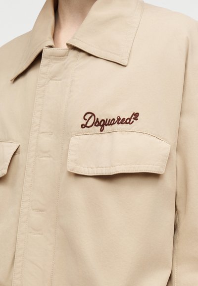 Μπεζ μπουφάν Dsquared2 με μυτερό γιακά, κουμπιά μπροστά, τσέπες στο στήθος και κεντημένο λογότυπο  με καφέ κλωστή. Ομαλή υφή υφάσματος.