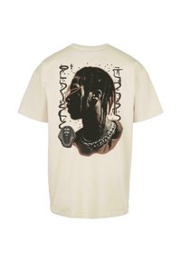 Cream-colored t-shirt featuring a graphic of a profile silhouette, chains, and an Egyptian motif on the back, with textured details and splashes.