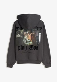 Sweat à capuche gris avec un imprimé graphique de Frankenstein et le texte « Les monstres jouent à Dieu » en lettres grasses noires. Matière en coton, coupe décontractée.