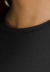 Svart bomullsskjorta med rundad halsringning och mjuk textur, som visar det övre tyget och den omgivande hudtonen.