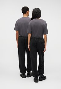 Δύο άτομα γυρισμένα πλάτη, φοράνε σκούρα γκρι T-shirts και μαύρο παντελόνι φόρμας με ελαστικά τελειώματα, με διακριτική υφή και άνετη εφαρμογή.