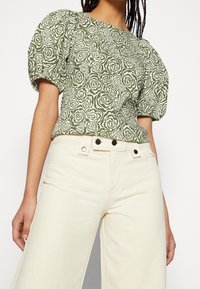 Zielona bluzka w kwiaty z bufiastymi rękawami, zestawiona z kremowymi spodniami z szerokimi nogawkami, z zapięciem na guziki w pasie.