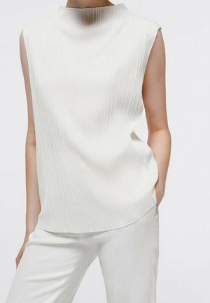Haut sans manches blanc avec des plis verticaux, col haut et fentes latérales. Texture lisse, associé à un pantalon sur mesure assorti.